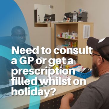 A doctor talking to a patient seated at a desk inside a clinic, with medical supplies on a shelf behind them.